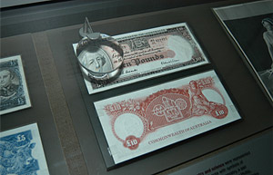 Collectible banknotes displayed in a cabinet, with a magnifying glass.